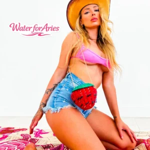 A woman in a pink bikini top and denim shorts with watermelon design, posing confidently.