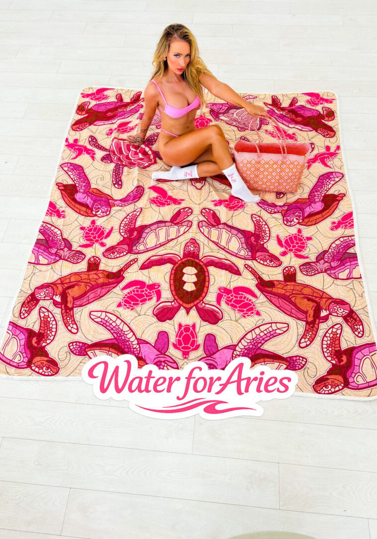 A colorful pink and orange towel with a zodiac Aries design and a doll sitting on it.